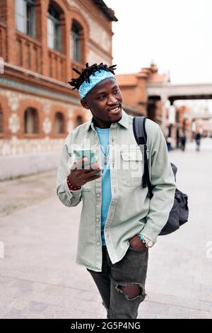 Bell'uomo africano che cammina per strada e usa il suo cellulare. Foto Stock