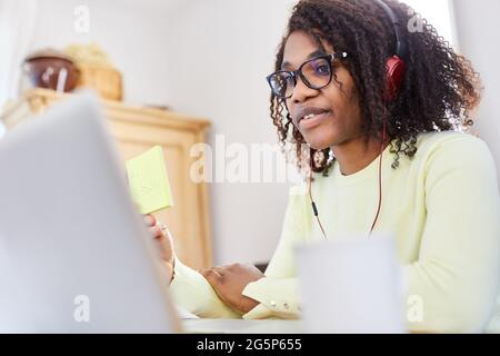 Donna d'affari africana che usa note appiccicose sul computer durante una videoconferenza nell'ufficio domestico Foto Stock