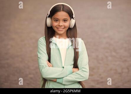un bambino allegro indossa auricolari con canzone musicale all'aperto godendo della melodia, di nuovo a scuola Foto Stock