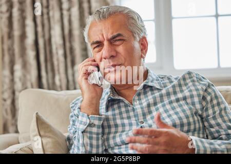 Frustrato uomo maturo che riceve chiamata telefonica indesiderata a casa Foto Stock