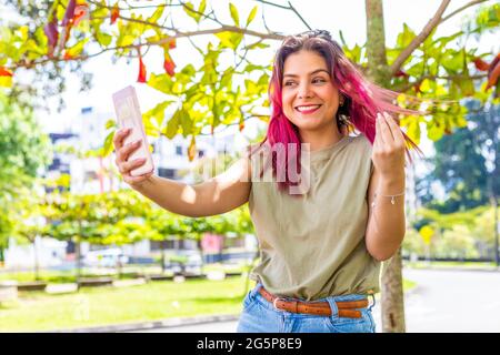 giovane ragazza nel parco sotto un albero che prende un selfie con il suo smartphone Foto Stock