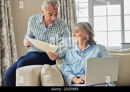 Sorridente coppia matura a casa rivedere le finanze nazionali su notebook Foto Stock
