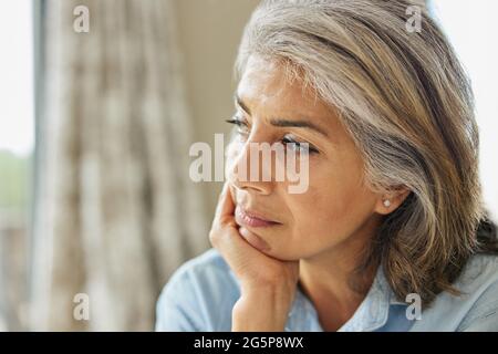 Testa e spalle Tiro di donna matura pensierosa che guarda fuori dalla finestra a casa Foto Stock