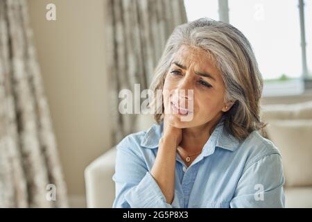 Donna matura a casa che soffre di dolore muscolare o Ache nel collo Foto Stock