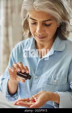 Donna matura seduta sul divano a casa prendendo farmaci Foto Stock