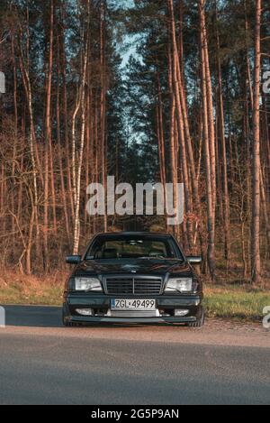 Goleniow, Polonia - 20 aprile 2021: Vecchia Mercedes Benz classe C (modello W202) sintonizzata nera vicino alla foresta. Icona berlina compatta e di lusso degli anni '90. Verticale Foto Stock