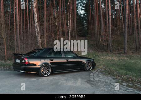 Goleniow, Polonia - 20 aprile 2021: Vecchia Mercedes Benz classe C (modello W202) sintonizzata nera vicino alla foresta. Icona berlina compatta e di lusso degli anni '90. Vista laterale Foto Stock