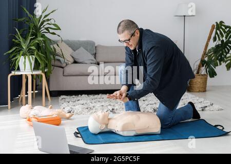 Paramedico che dimostra il primo soccorso sul manichino durante l'addestramento da solo in salotto. L'istruttore mostra CPR sulla bambola da allenamento Foto Stock