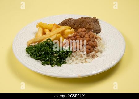 Tipico piatto basico brasiliano con riso, fagioli, bistecca, patatine fritte e cavolo brasato in un piatto bianco in vista Foto Stock