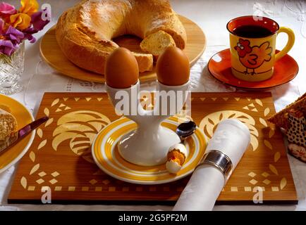 Tavolo per la colazione con doppia tazza di uova, uova in bolo, pane, chick con cucchiaio, tovagliolo, serviette, anello d'argento, piselli dolci in vaso di vetro tagliato, caffè nero in tazza Foto Stock