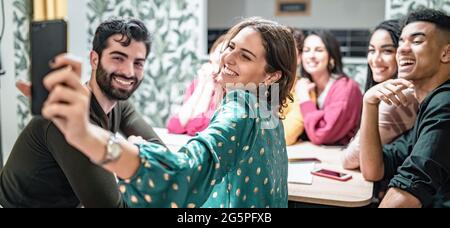 Incontro di giovani migliori amici che prendono uno smartphone selfie al chiuso seduto sul salotto insieme. Foto Stock