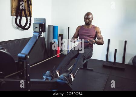 Allenati in palestra con l'afroamericano, utilizzando la vogatrice Foto Stock