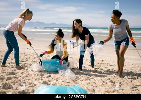 Gruppo vario di amici femminili che raccolgono i rifiuti dalla spiaggia Foto Stock