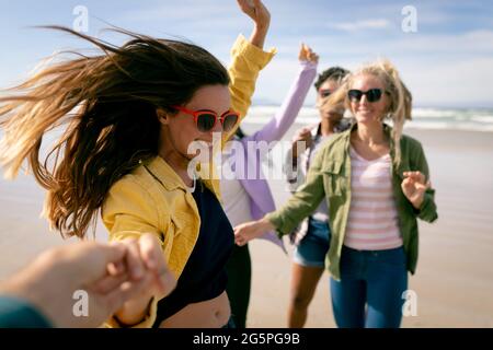 Felice gruppo di diverse amiche che si divertono, camminando lungo la spiaggia tenendo le mani e ridendo Foto Stock