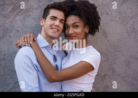 ritratto di una giovane coppia multirazziale abbracciata teneramente contro un wal concreto Foto Stock