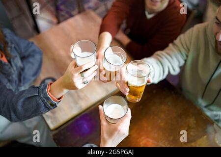 Incontro di migliori amici seduti nel pub alzando bicchieri di birra in un brindisi celebrativo. Giovani che si divertono a bere bevande alcoliche Foto Stock