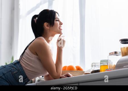 felice giovane e bruna donna che guarda via in cucina Foto Stock