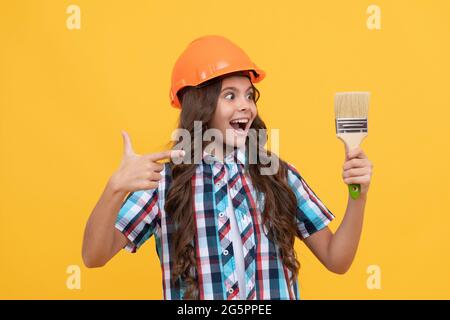 stupito teen ragazza che punta il dito sulla pittura pennello. bambino pittore in casco. Foto Stock