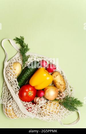 Borsa trendy con verdure fresche e verdi su sfondo verde chiaro: Patate, pomodori, cipolla, peperone. Zero sprechi di vita sostenibile Foto Stock