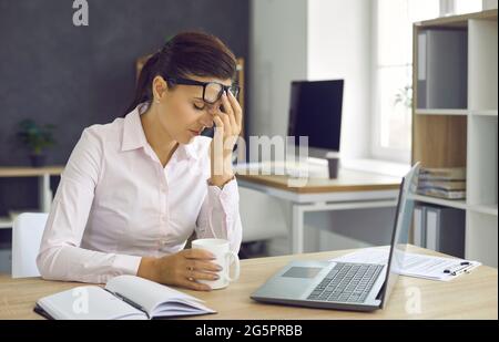 Giovane donna stanca che riposa durante una pausa dal lavoro d'ufficio, sollevando i suoi occhiali Foto Stock