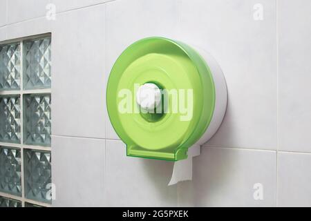 Porta rotolo di carta igienica verde in plastica con carta bianca sulla parete in piastrelle del bagno Foto Stock