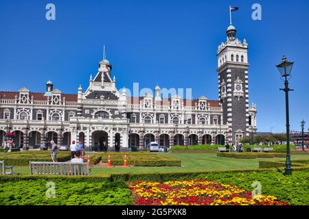 L'architettura esterna ornata della stazione ferroviaria a Dunedin, Isola del Sud, Nuova Zelanda, con aiuole di fiori di fronte Foto Stock