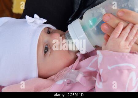 Primo piano su una mano del neonato che tiene la mano della mamma mentre si allatta il latte da un biberon Foto Stock