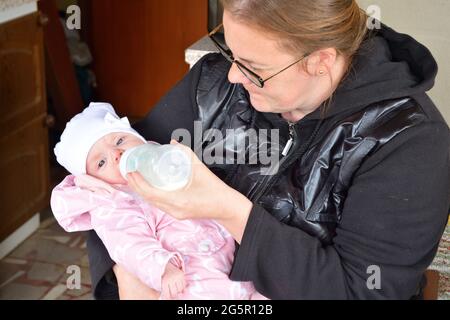 Una madre nutre il suo bambino con il latte da un biberon Foto Stock