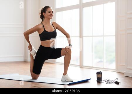 Giovane donna che allunga la gamba che si esercita sul tappetino yoga Foto Stock