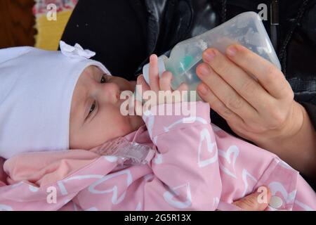 Primo piano su una mano del neonato che tiene la mano della mamma mentre si allatta il latte da un biberon Foto Stock