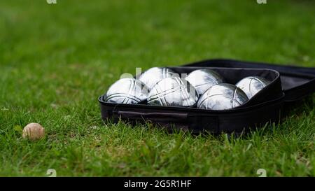 Set di bocce con sei palline di metallo in una custodia nera su erba verde. Gioca nel tuo giardino durante la quarantena. Foto Stock