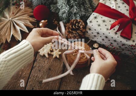 Mani legate nastro su biscotti di Natale farinata d'avena su rustico tavolo di legno con eleganti decorazioni festive. Immagine di natale atmosferica. Biscotti sani, Foto Stock