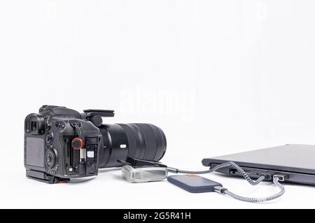 workstation di elaborazione fotografica con un computer portatile, una dslr, un lettore di schede cf e un'unità disco ssd su sfondo bianco con spazio per la copia Foto Stock