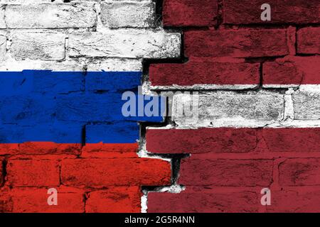 Concetto del rapporto tra Russia e Lettonia con due bandiere dipinte su un muro di mattoni danneggiato Foto Stock