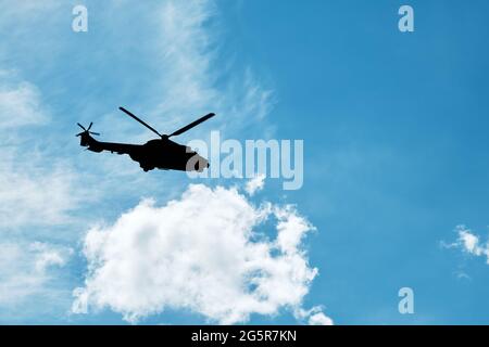 Silhouette di un elicottero che vola sullo sfondo blu del cielo con nuvole. Foto Stock