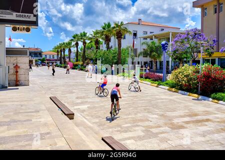 Urla, İzmir, Turchia - Giugno 2021: Bambini in bicicletta e persone che camminano nella piazza Urla di İzmir, Turchia. Foto Stock