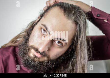 ritratto di un giovane uomo d'affari medio orientale con barba e capelli lunghi che regolano i capelli Foto Stock