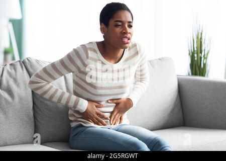 Stomaco Ache. Giovane donna africana che soffre di dolore addominale acuto a casa Foto Stock