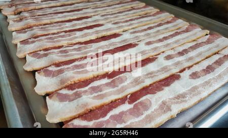 Strisce di pancetta grezza allineate su un forno rack, vista ad angolo basso con profondità di campo poco profonda e messa a fuoco in primo piano. Foto Stock