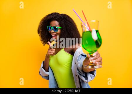 Ritratto fotografico di bella ragazza che mostra il cocktail delle dita in estate festa isolata giallo brillante sfondo Foto Stock