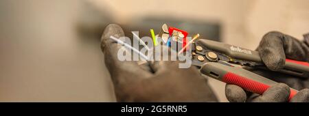 Spelafili. L'elettricista pulisce l'isolamento protettivo dal filo utilizzando uno spelafili. Il processo di collegamento dei fili. Primo piano Foto Stock