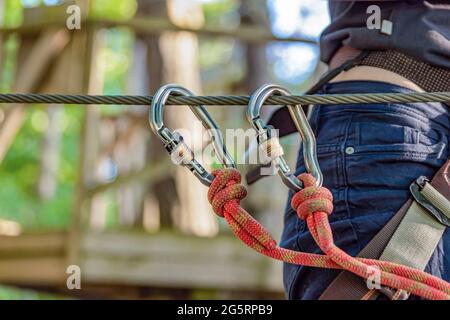 Forest Adventure Park. La donna digiuna il suo moschettone e usa l'attrezzatura per arrampicarsi. Superare gli ostacoli nel parco avventura forestale. Banner per Foto Stock