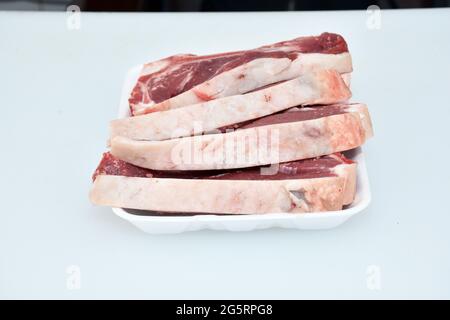 bistecca di agnello in piatto su sfondo bianco, carne di montone cruda, cibo biologico, macellaio tagliato Foto Stock