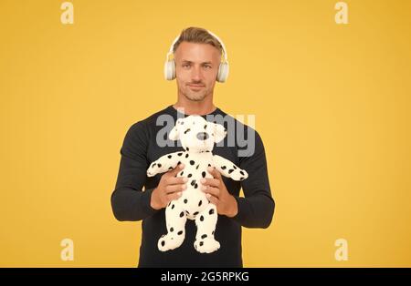 Bell'uomo di mezza età tenere morbido cane giocattolo per giocare ascoltando la musica in cuffia sfondo giallo, adozione Foto Stock