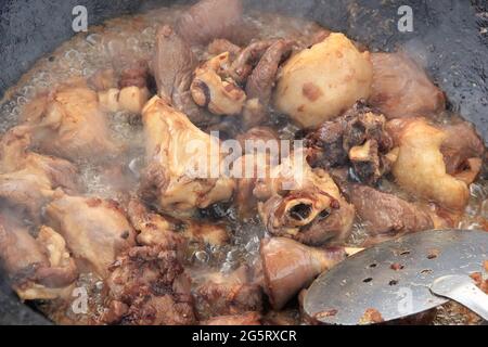 Grandi pezzi di carne di agnello con stufato di agnello fritto in olio con bollicine in un calderone nero, cibo da cucina Foto Stock