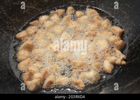 Grandi pezzi di manichino grezza di grasso di agnello vengono fritti in olio con bolle in un primo piano di calderone nero, cibo da cucina Foto Stock