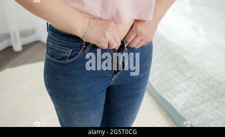 Closeup di giovani donne sconvolse dopo il montaggio e cercando di buttare su piccoli jeans. Concetto di peso eccessivo, femmina obese, dieta e sovrappeso Foto Stock