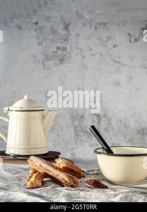 Tipica colazione o spuntino spagnolo. Churros in sacchetto di carta con zucchero. Tazza con cioccolato e cucchiaio con cacao. Sfondo bianco. Foto Stock