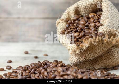 Caffè arrosto in un sacco di burlap su sfondo di legno. I chicchi di caffè sono caduti su uno sfondo di legno. Attività di caffè. Raccolta del caffè. Copysp Foto Stock