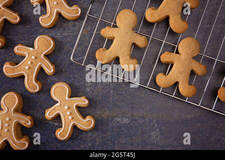 Batch di Gingerbread gente Cookies mezzo Iced e mezzo incompiuto su un tavolo di ardesia Foto Stock